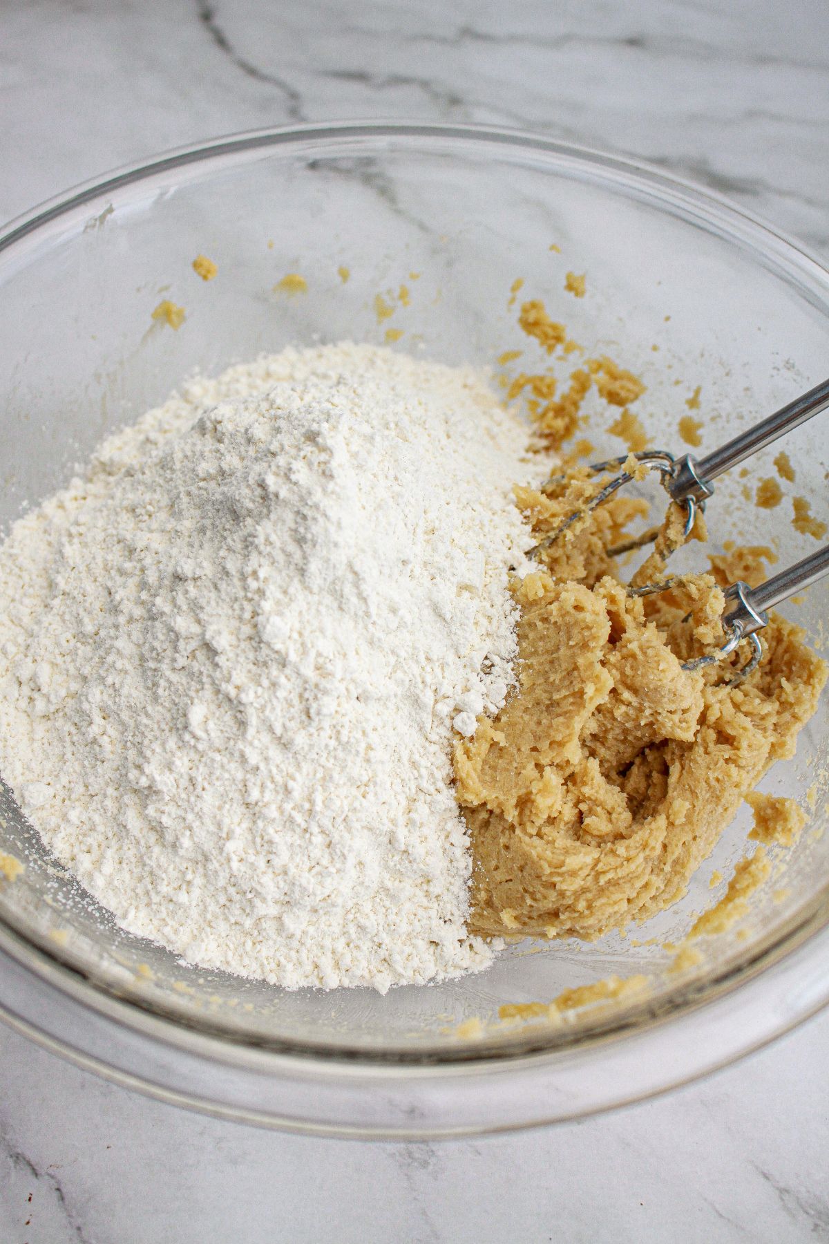 dry ingredients being mixed into wet ingredients in a mixing bowl with a hand mixer.