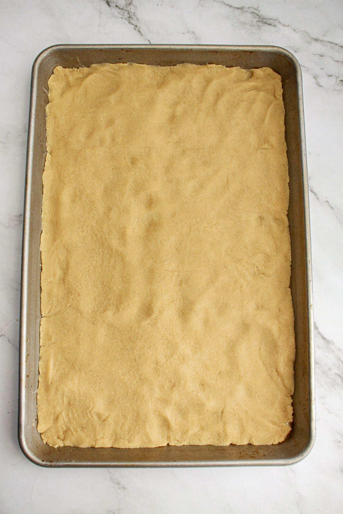 crust mixture being pressed into a thin layer in the a rimmed baking sheet.