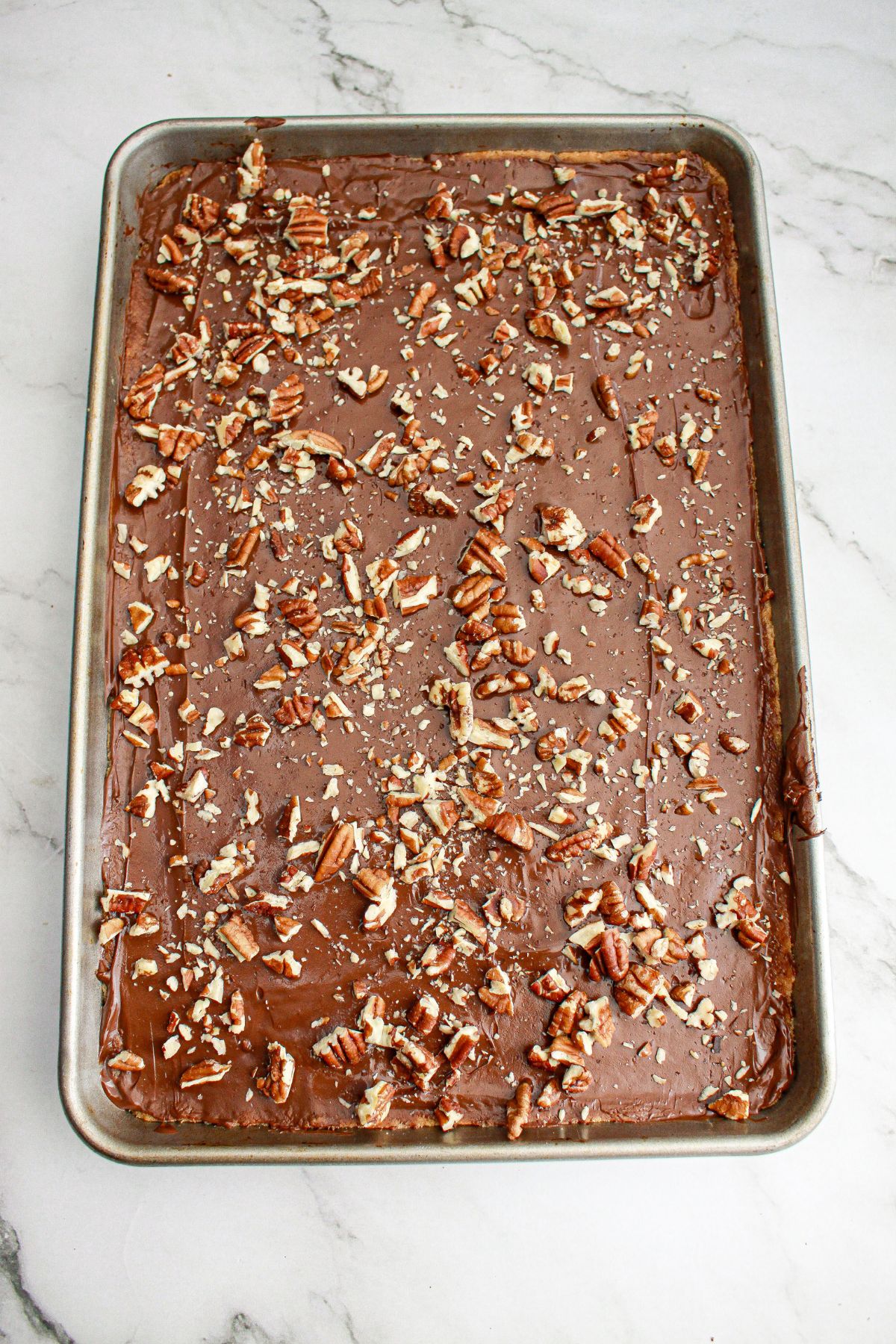 toasted pecans being sprinkled on top of toffee in a pan