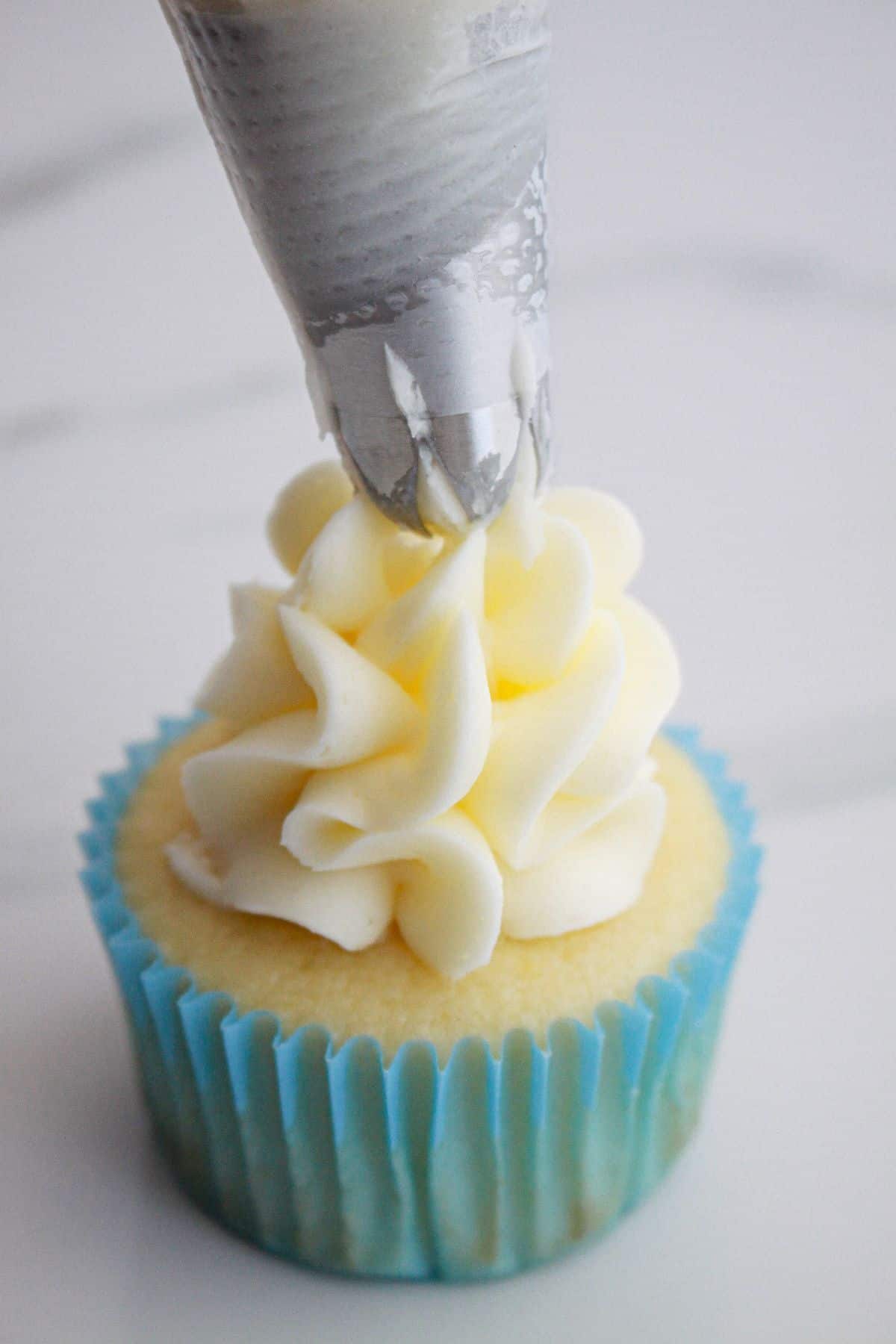 frosting being piped on top of a cupcake.