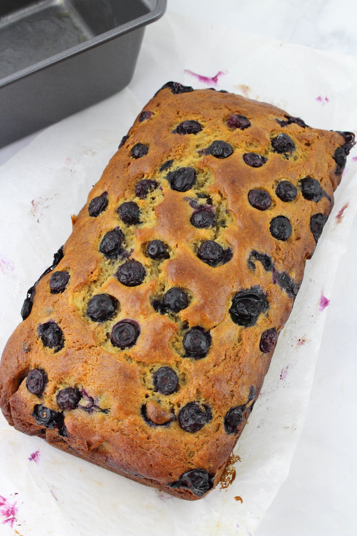 uncut blueberry bread loaf cooling on a counter.
