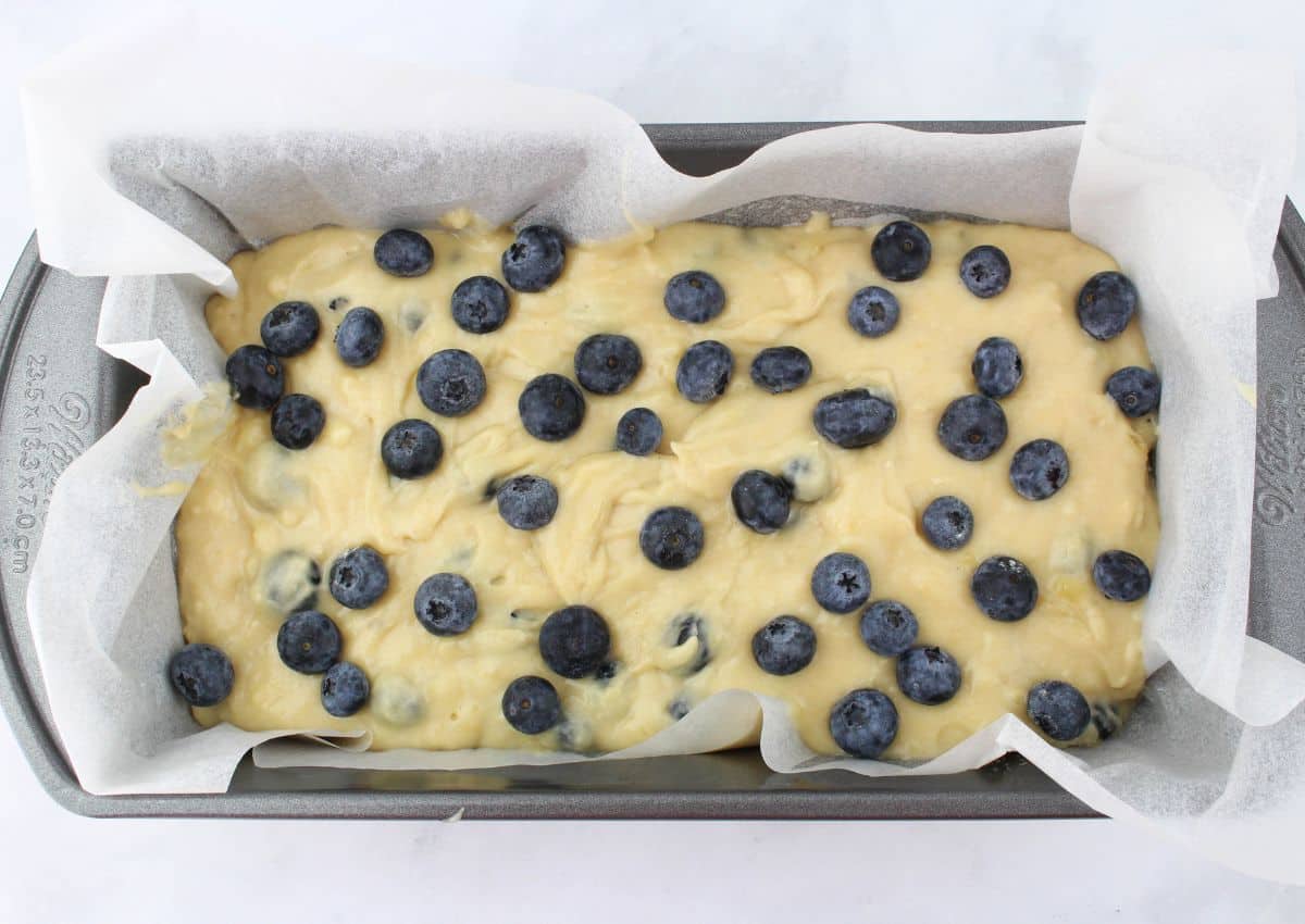 raw blueberry bread in a parchment lined loaf pan.