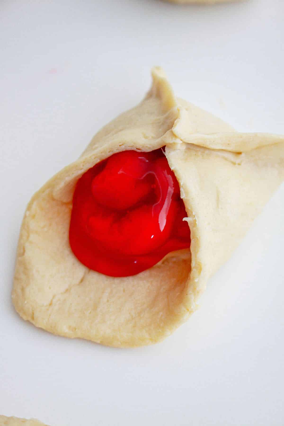 cream cheese and cherry pie filling being wrapped in crescent roll dough.
