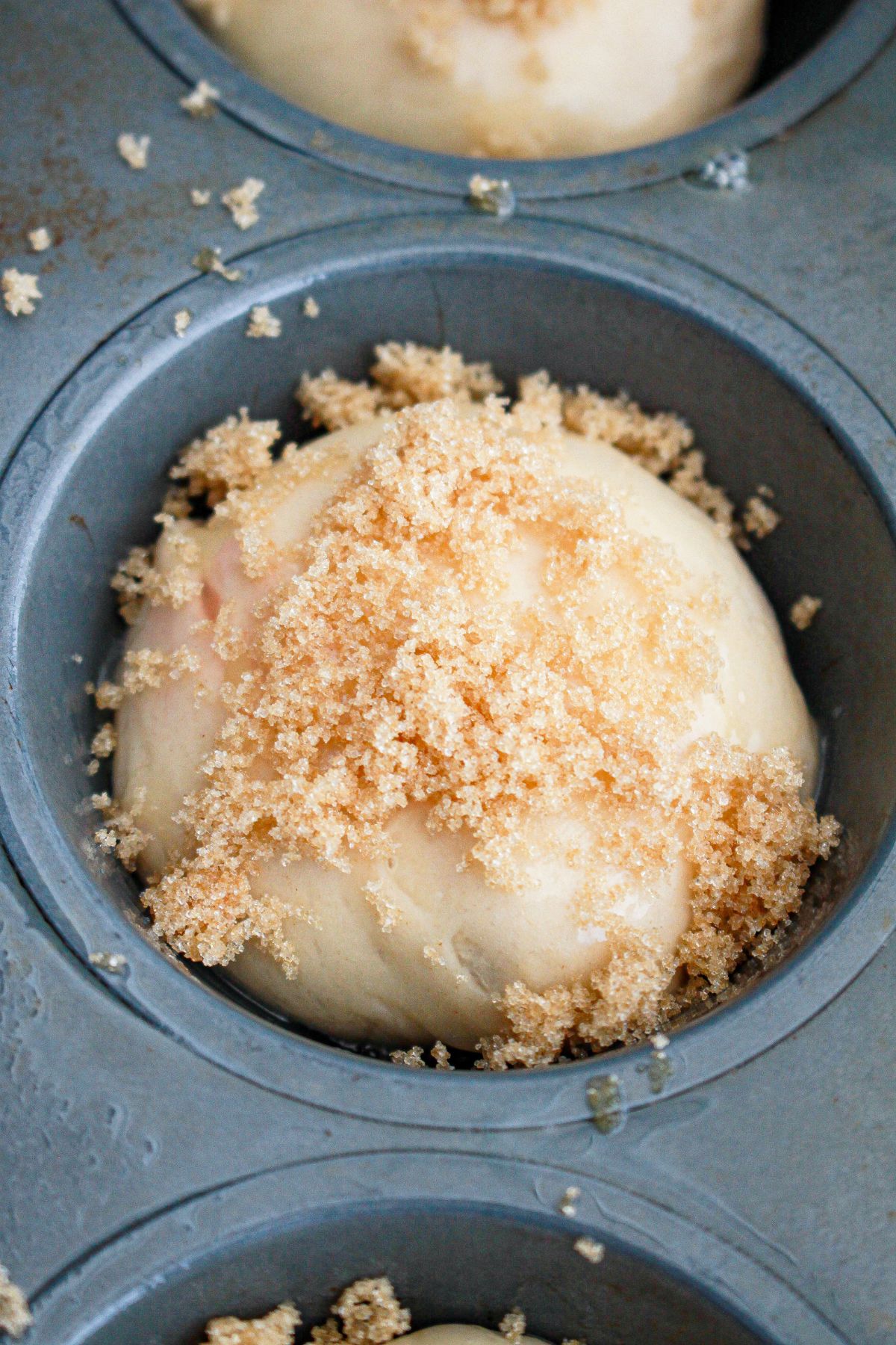 brown sugar being sprinkled on top of dough into a cupcake pan.
