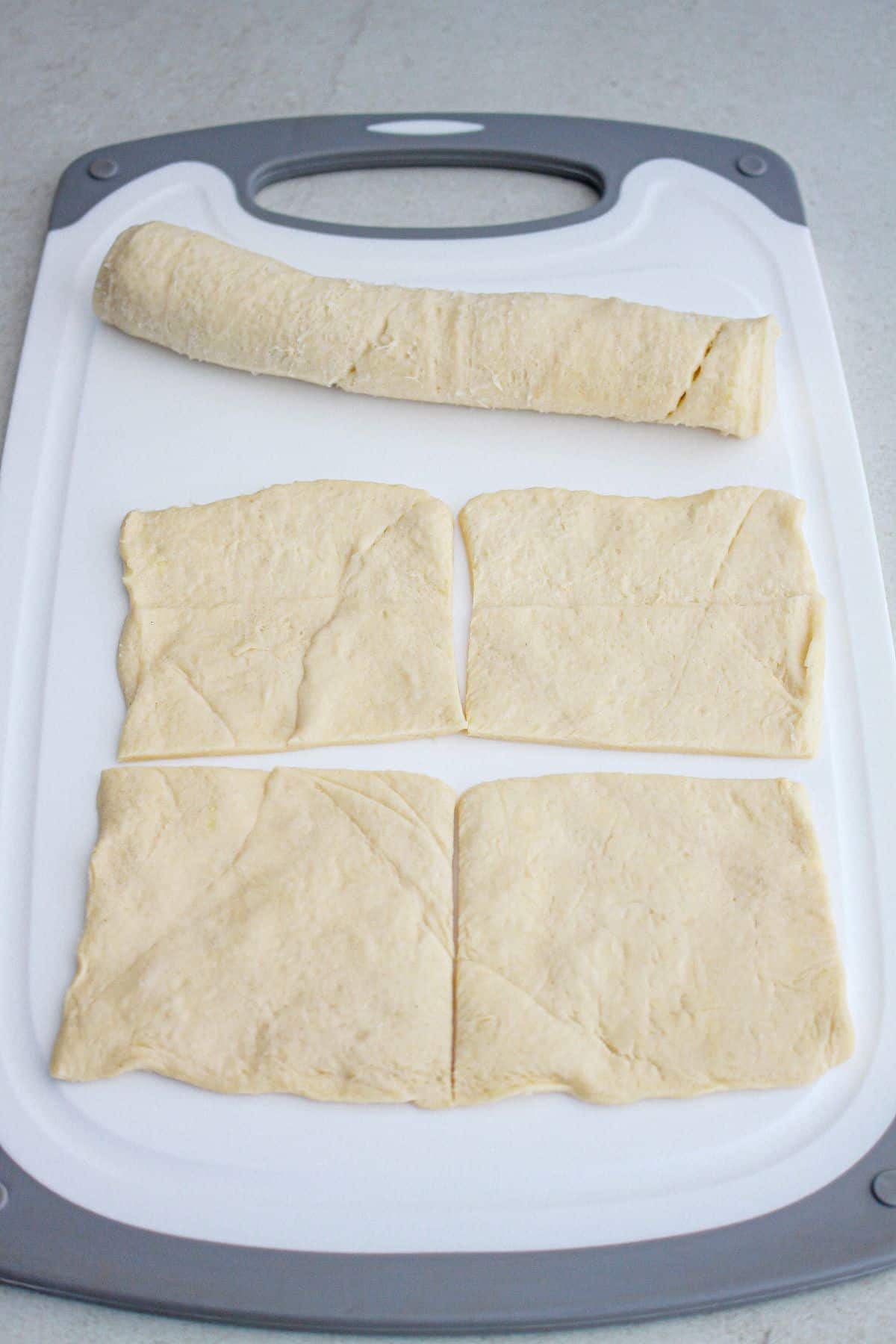 crescent roll dough being rolled out and pinch together on a cutting board.
