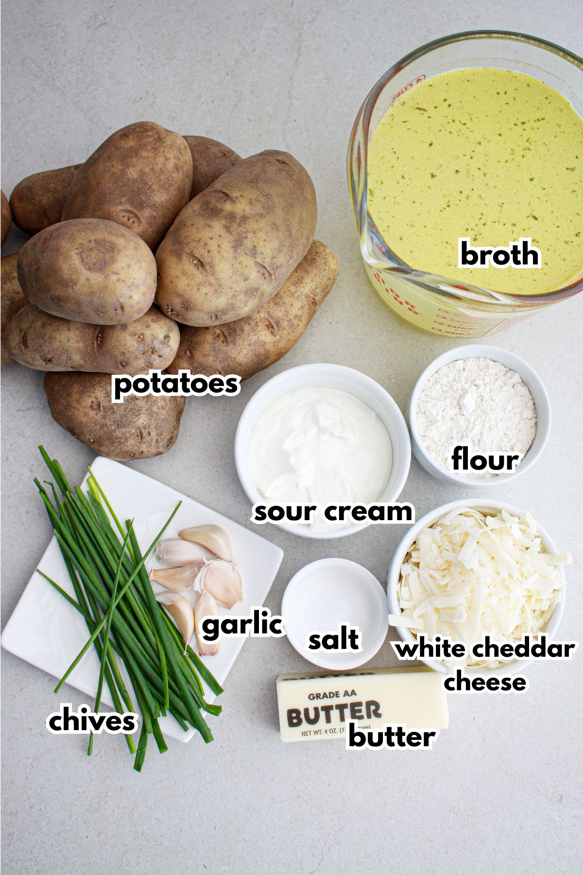bowls of potatoes, broth, chives, garlic, salt, sour cream, flour, white cheddar cheese and butter on a counter.