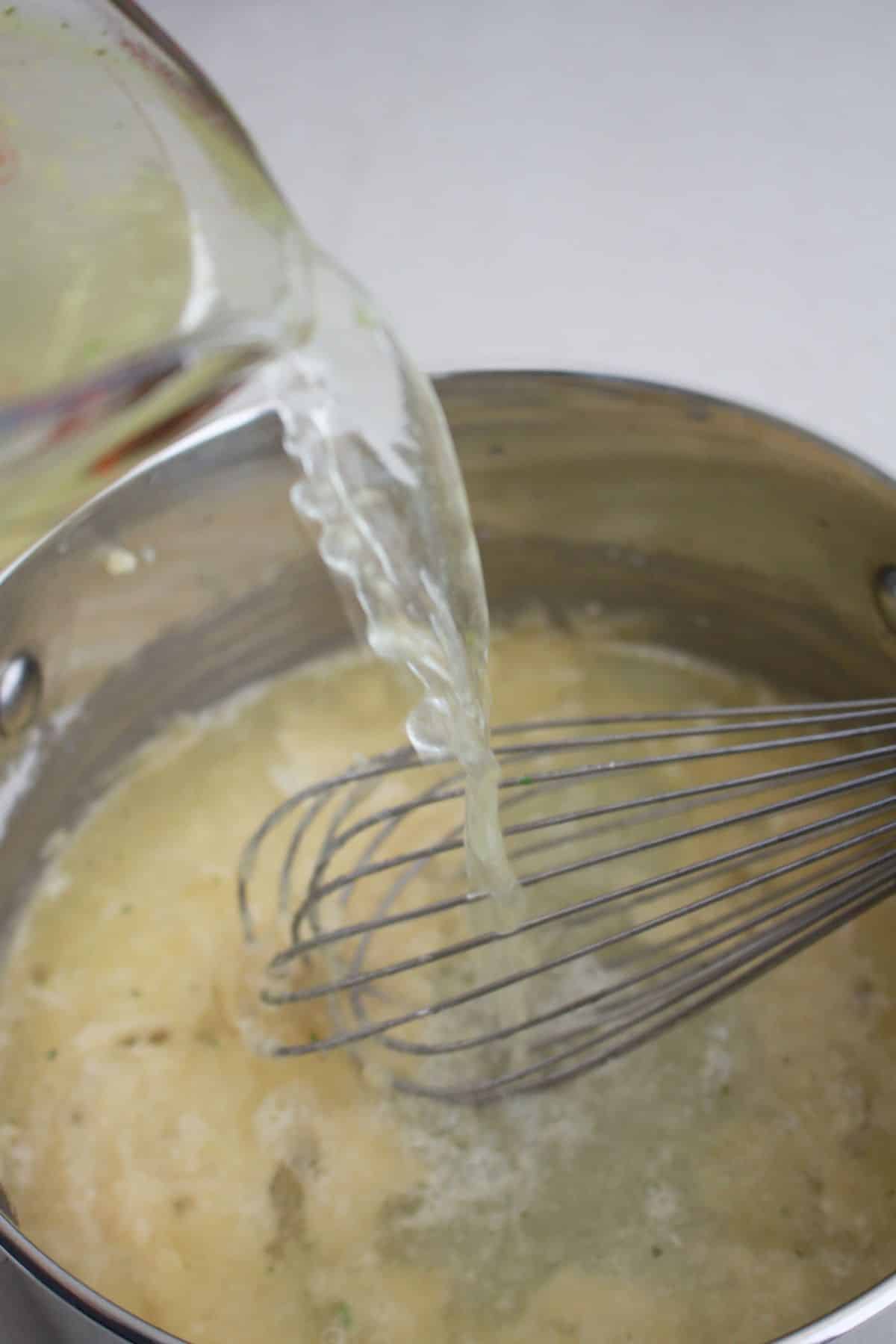 broth being added to a roux in a saucepan.