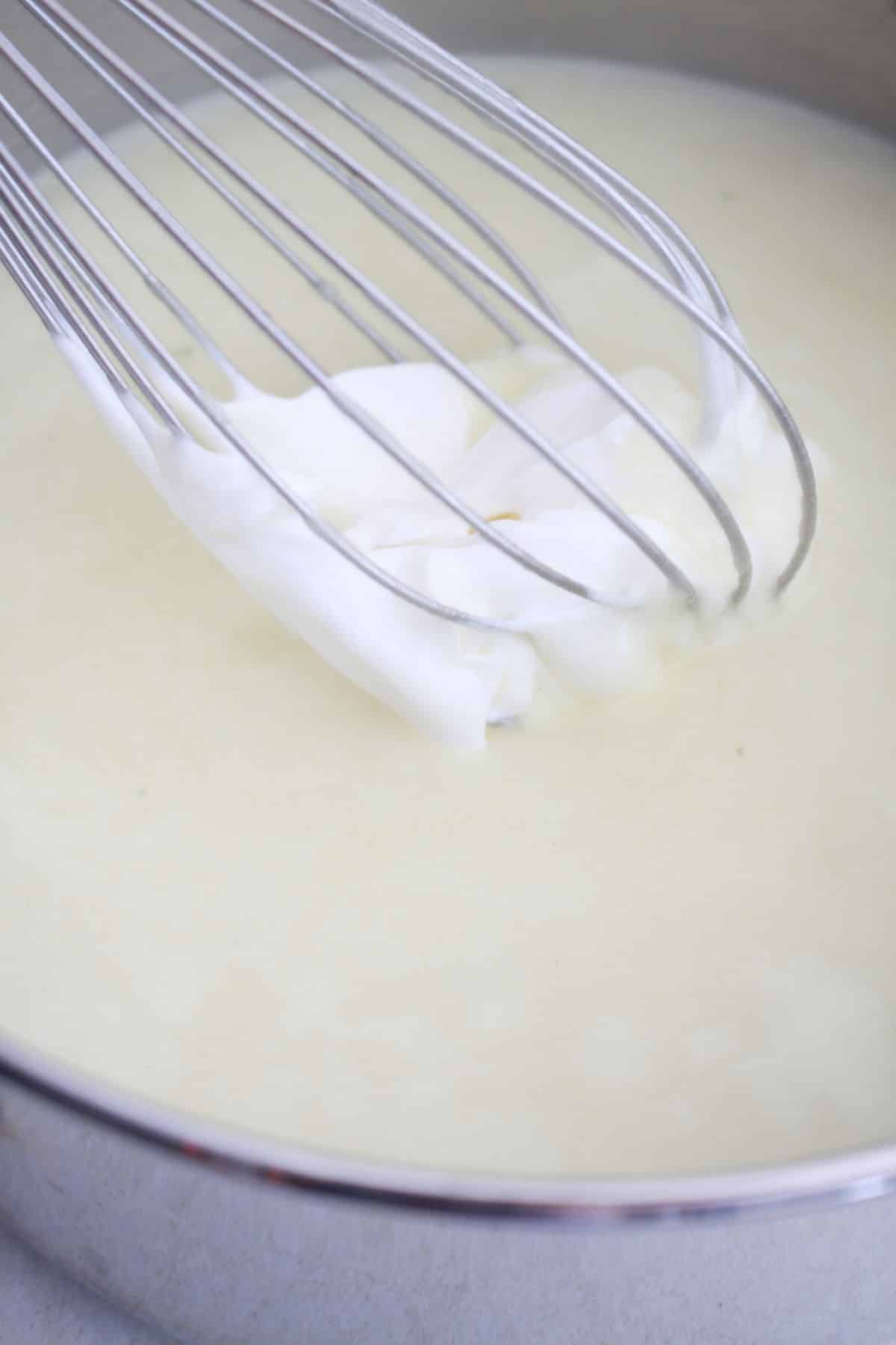 sour cream being added to a cream sauce in a pan.