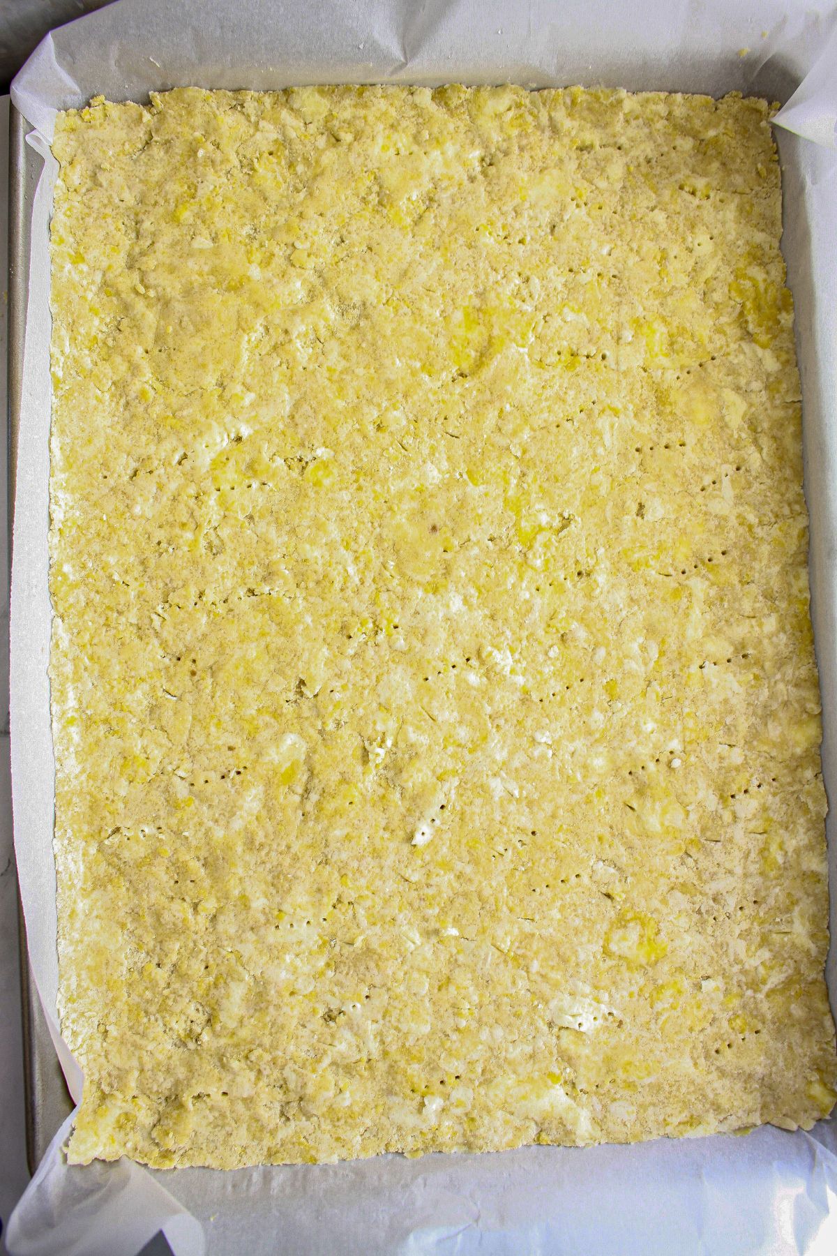 crust being pressed into a parchment lined baking dish.
