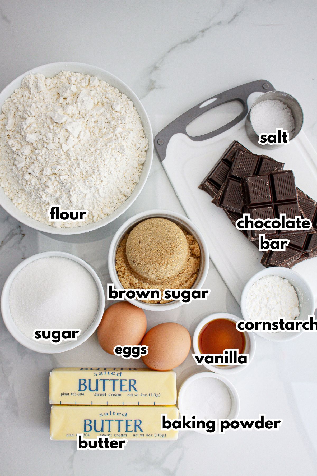 bowls of flour, sugar, brown sugar, eggs, chocolate bars, salt, butter, baking powder, vanilla, and cornstarch.