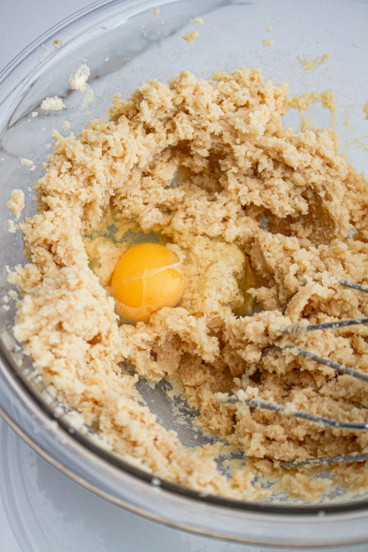 butter, sugar, eggs, and brown sugar being mixed in a glass mixing bowl.