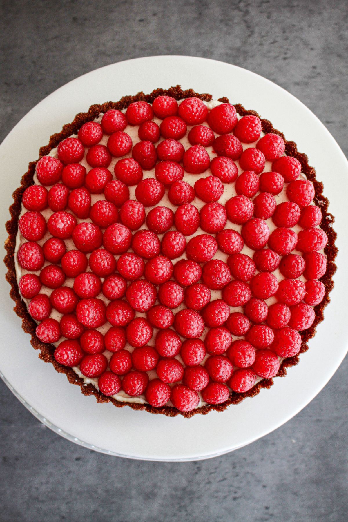 uncut chocolate raspberry tart on a cake stand.