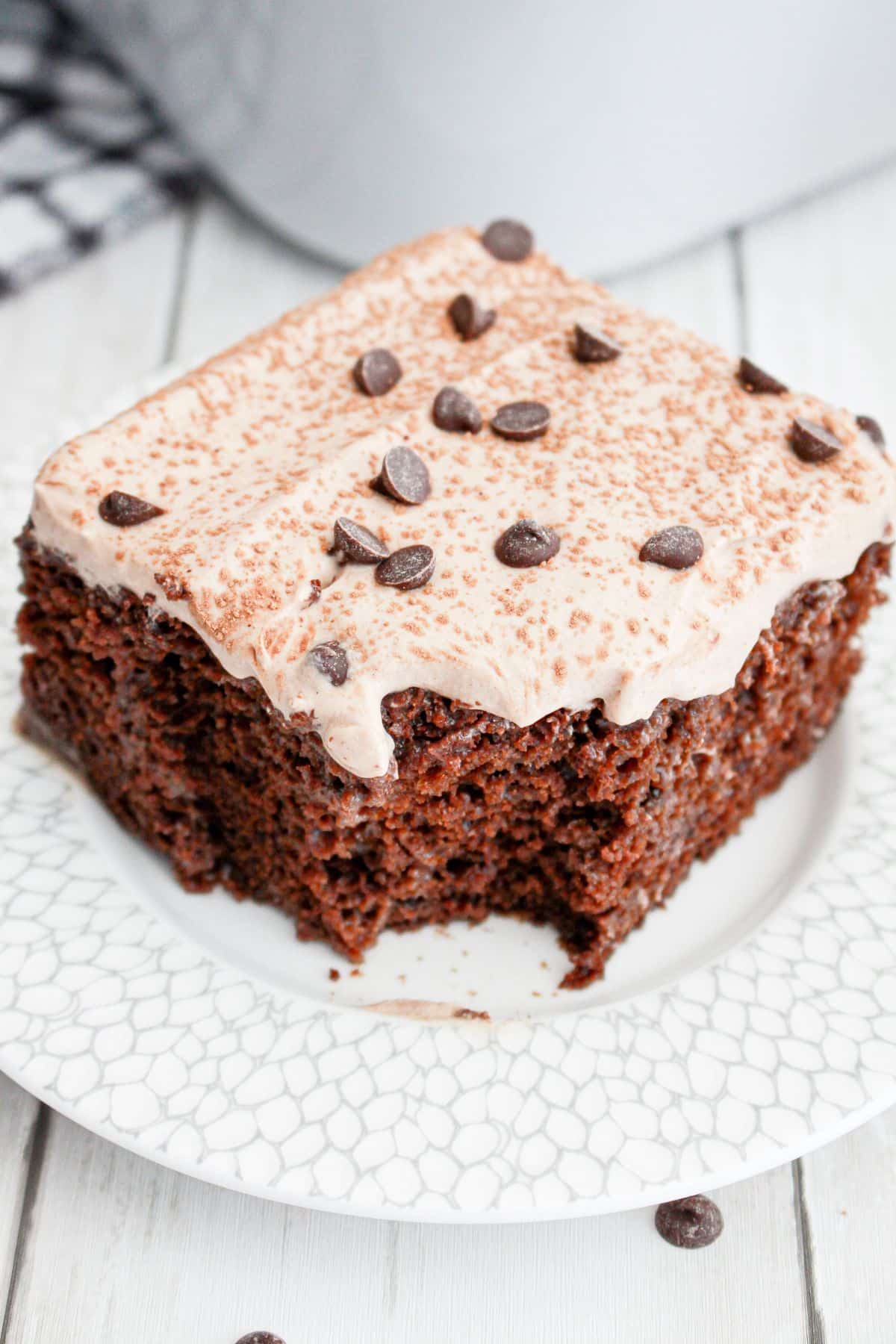 slice of chocolate tres leches cake on a plate with a bite missing.