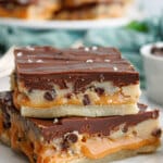 two salted caramel cookie dough billionaire bars stacked on top of each other on a counter.
