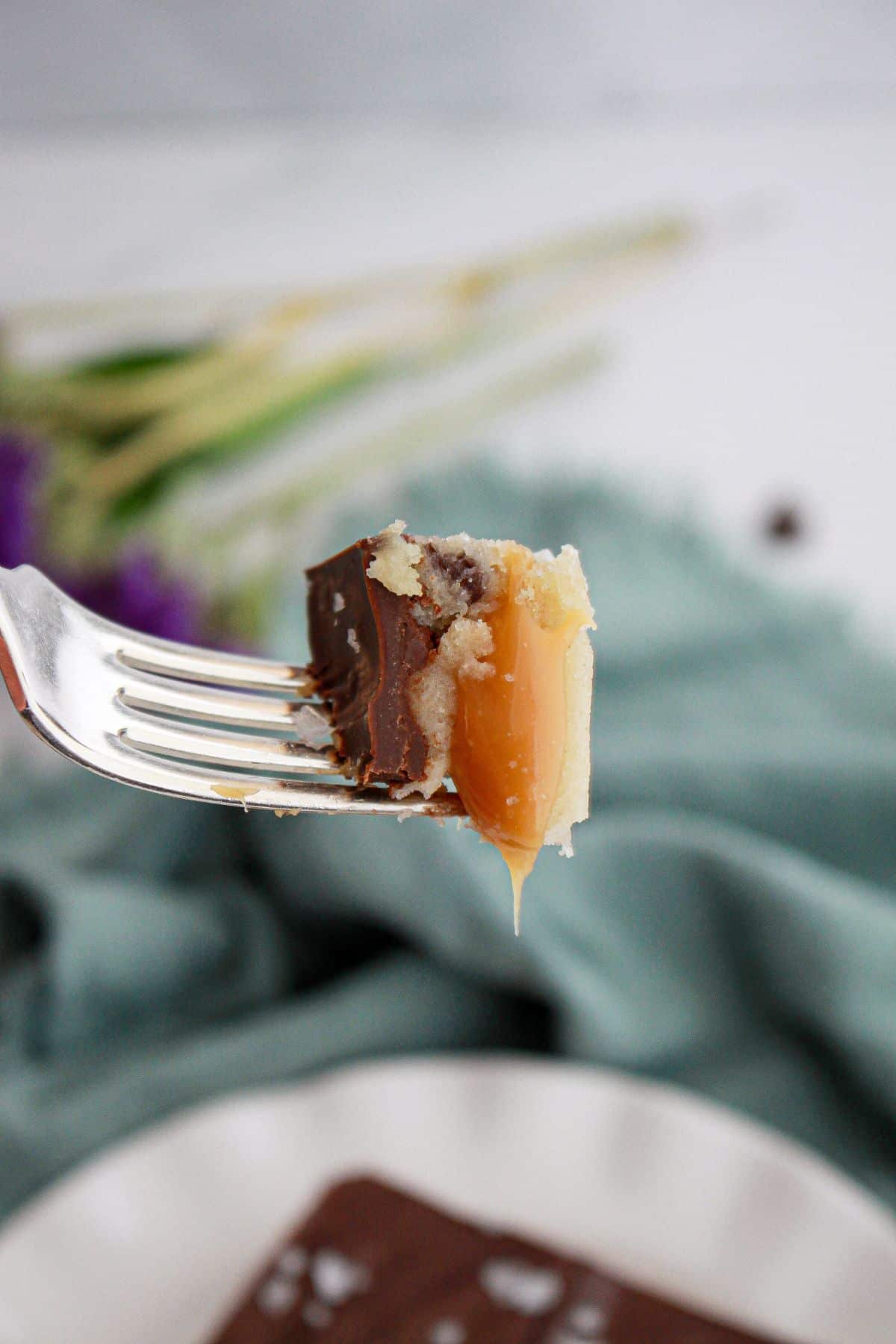 bite of salted caramel cookie dough billionaire bars on a fork held in the air.