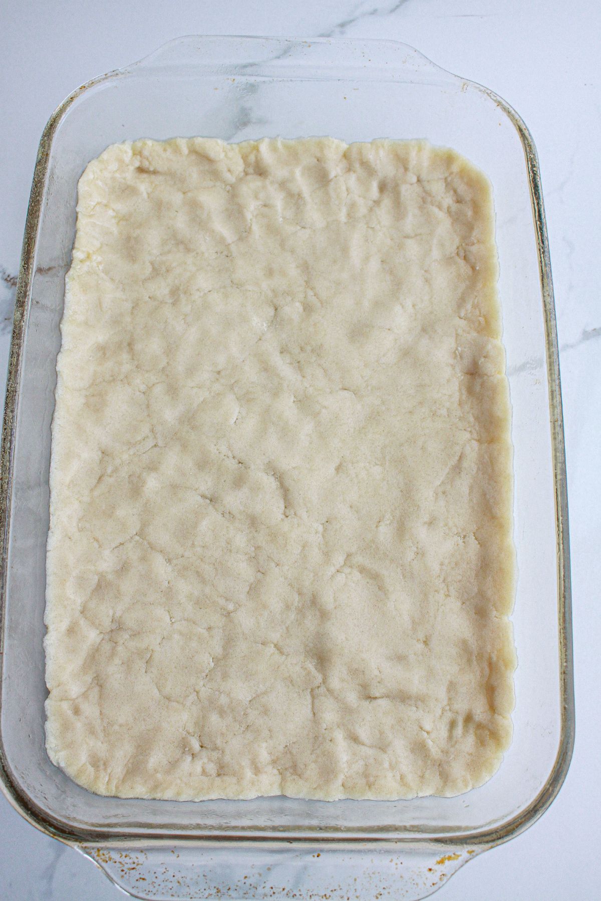 sugar cookie dough being pressed into the bottom of a glass baking dish.