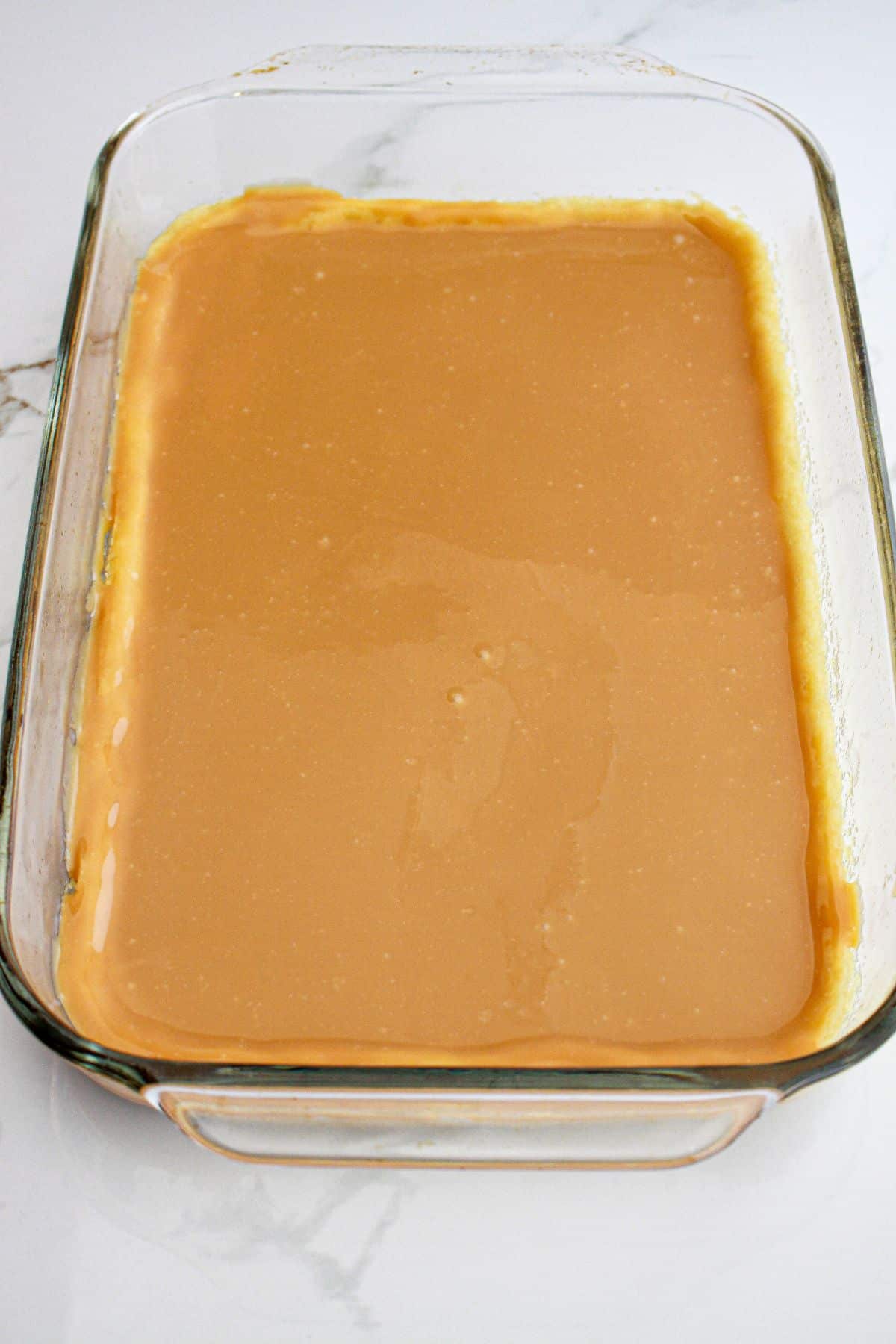 caramel being poured on top of a sugar cookie crust in a glass baking dish.