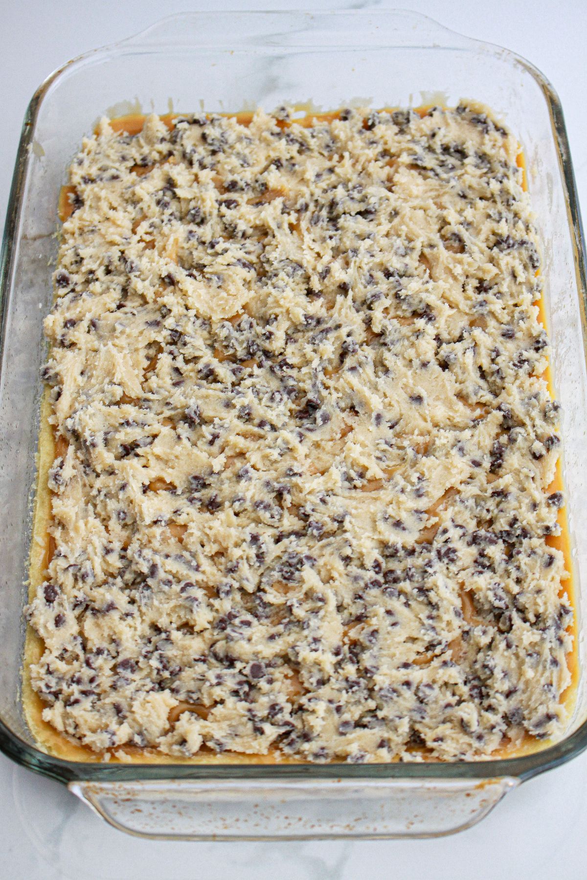 cookie dough being spread on top of a layer of caramel in a glass baking dish.