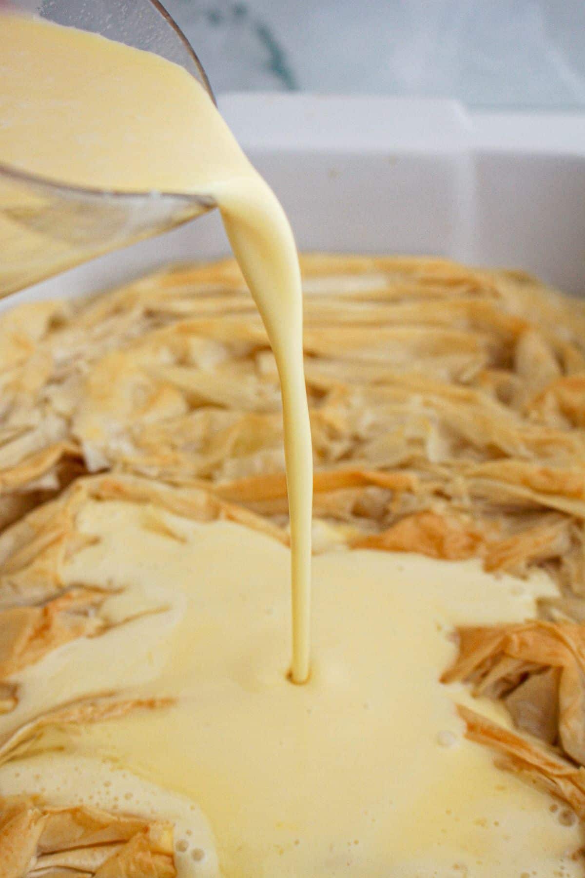 custard filling being poured on top of crinkle cake in a baking dish.