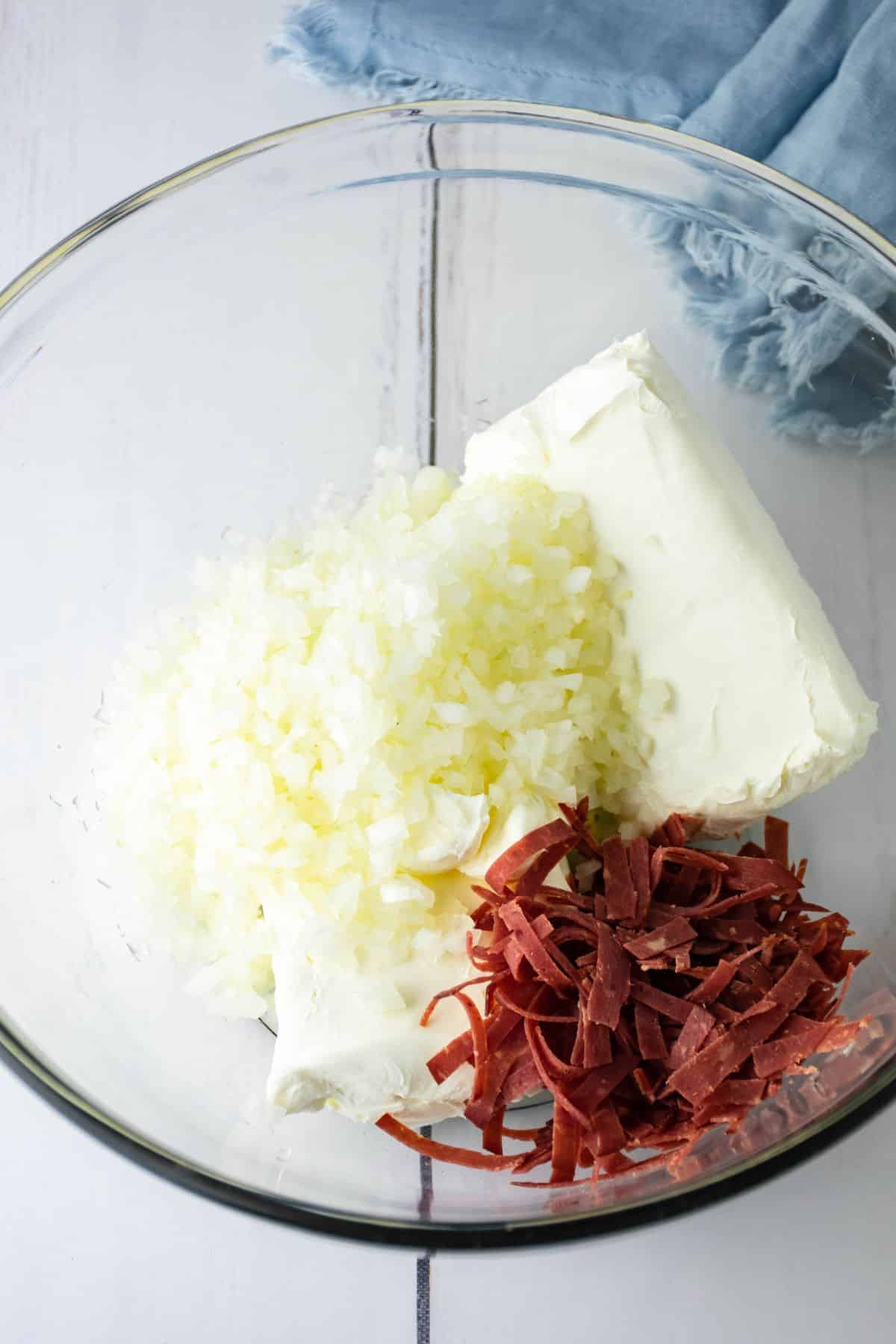 cream cheese, onions, and dried beef being mixed in a glass mixing bowl.