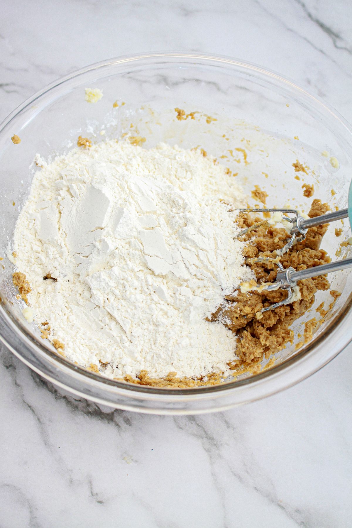 flour being added to butter and sugar in a mixing bowl.