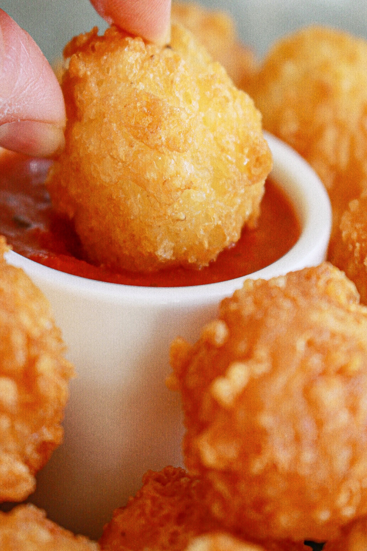 fried cheese bite being dipped into a small bowl of marinara sauce.