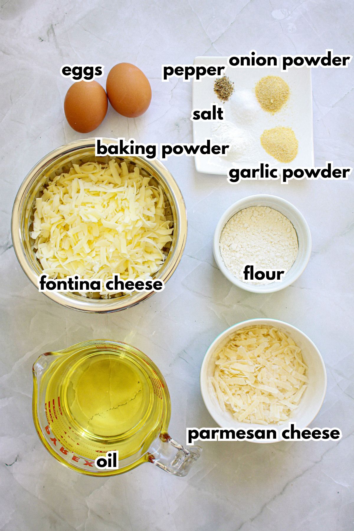 bowls of eggs, pepper, onion powder, salt, baking powder, garlic powder, fontina cheese, flour, oil and parmesan on a counter.