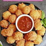 fried cheese bites stacked on a plate with a small bowl of marinara sauce in the center.