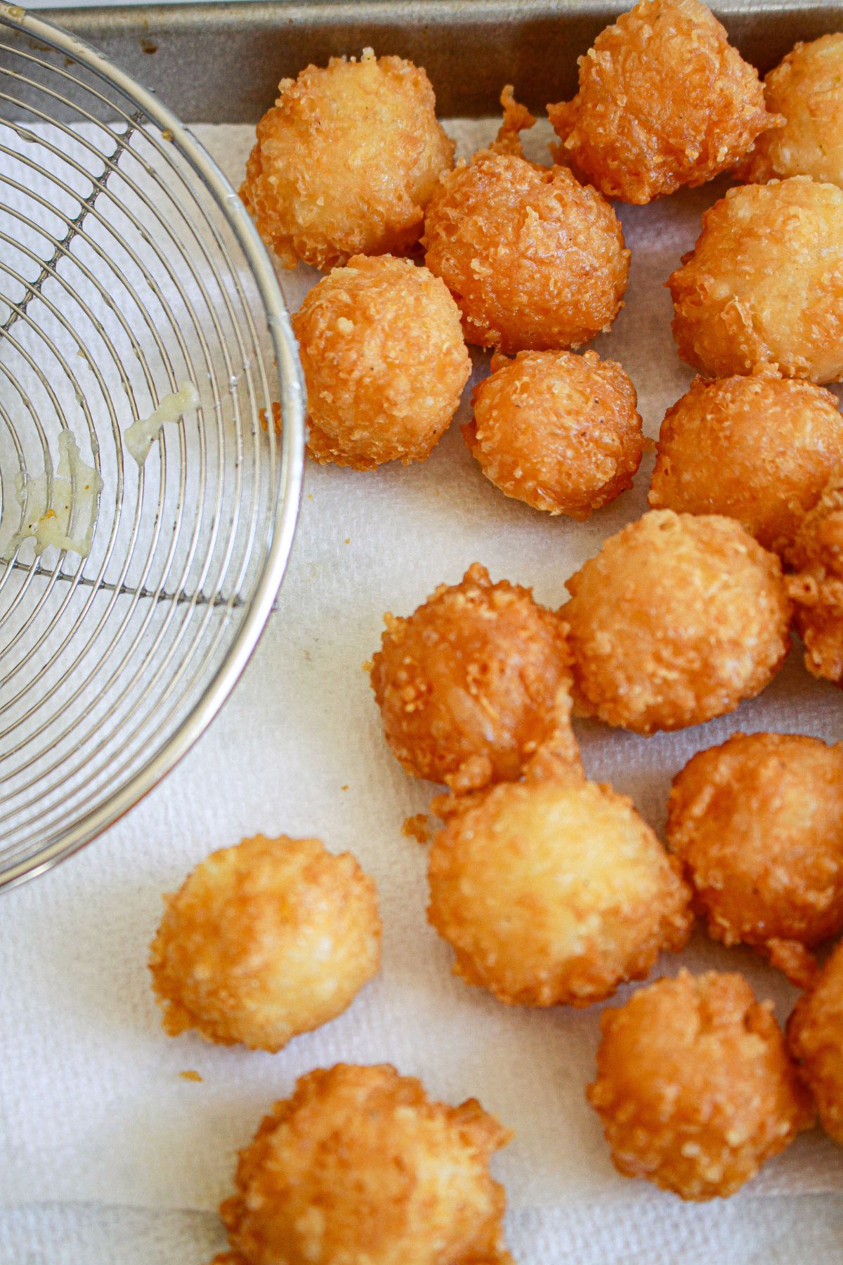 fried cheese bites being dried on a paper towel lined baking sheet.