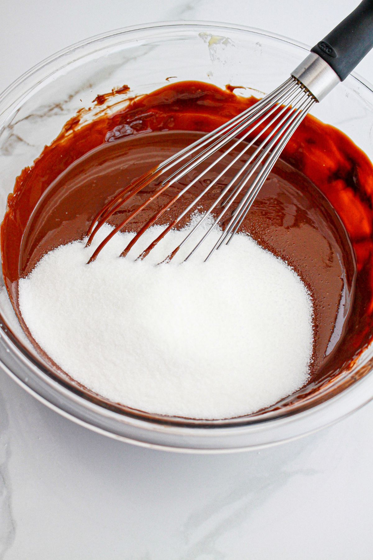 sugar being added to the brownie batter in a glass mixing bowl.