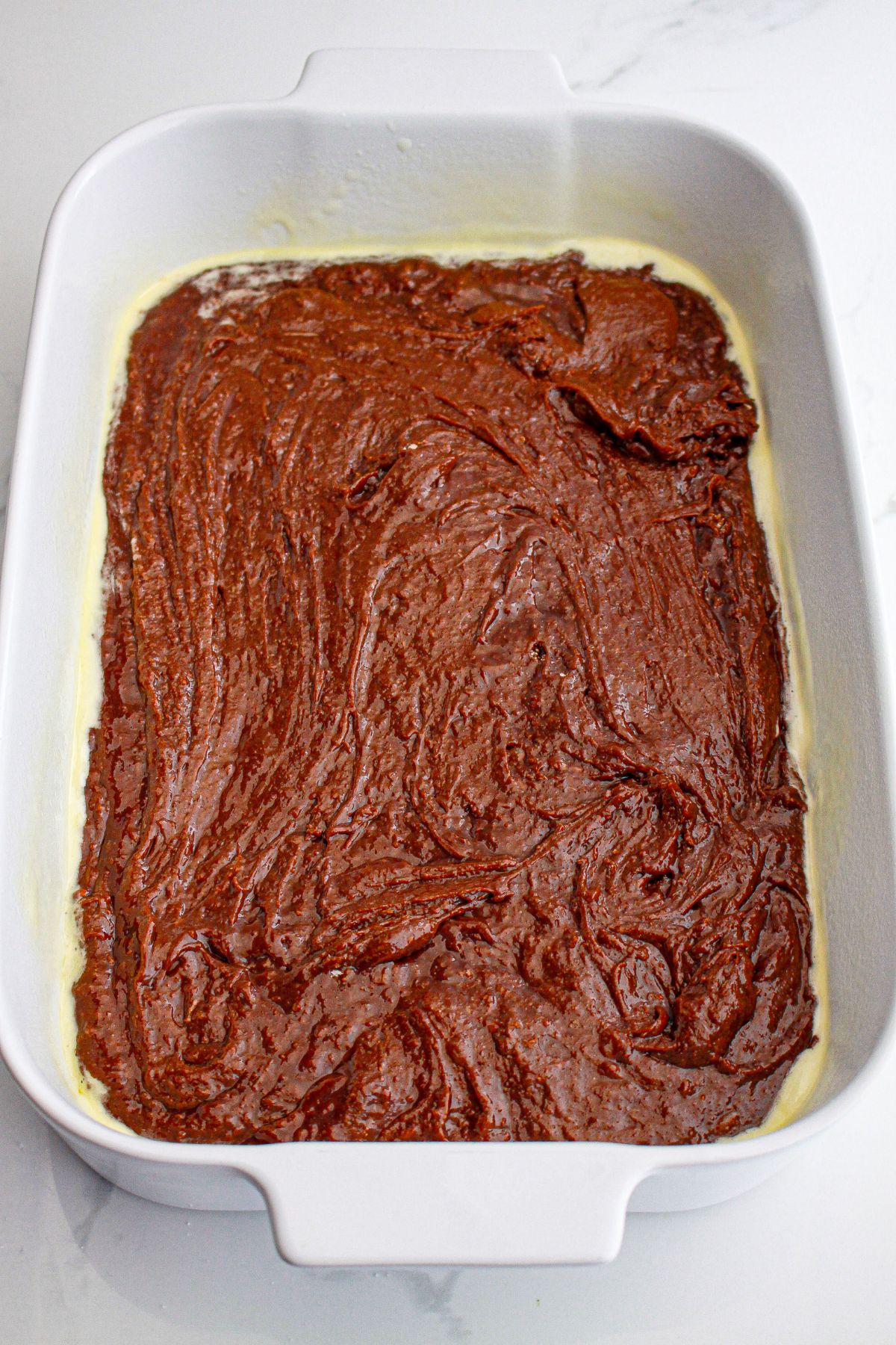 brownie batter being spread into a baking dish ready for the oven.
