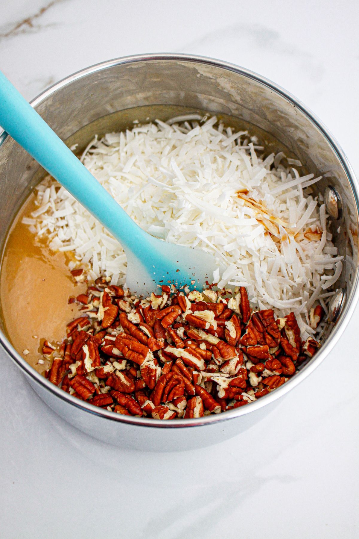coconut and pecans being stirred into caramel frosting.