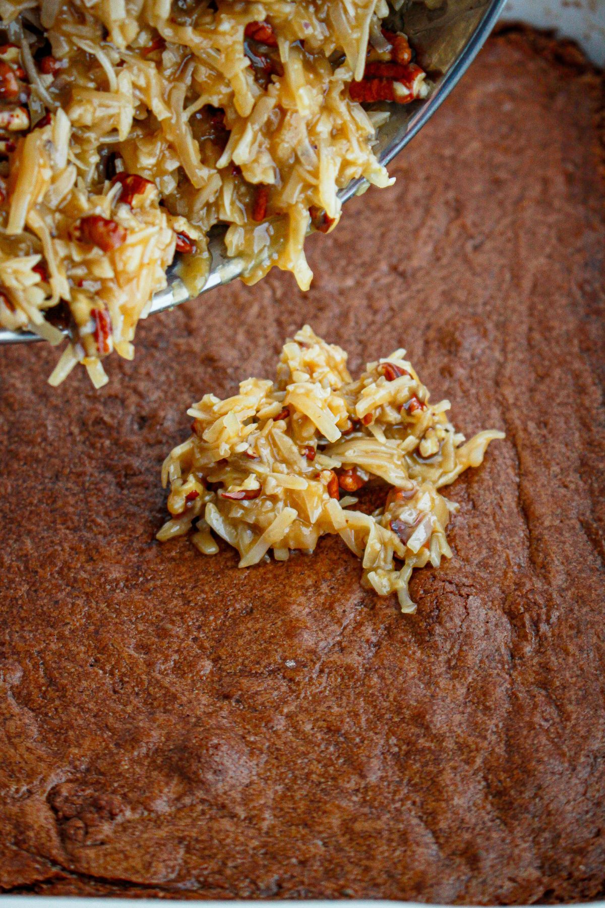 coconut pecan frosting being spread on top of baked brownies.