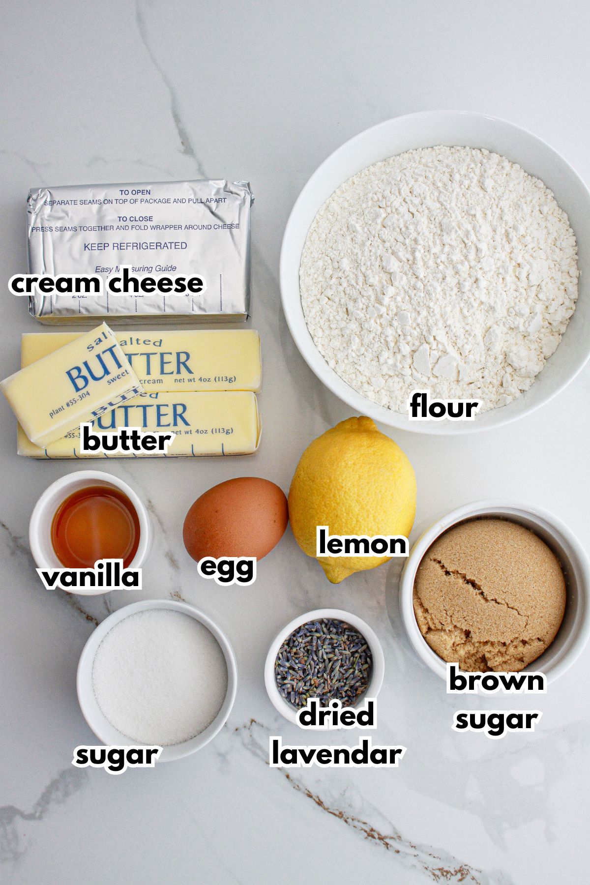 cream cheese, butter, flour, vanilla, egg, lemon, sugar, dried lavender, and brown sugar on a counter.