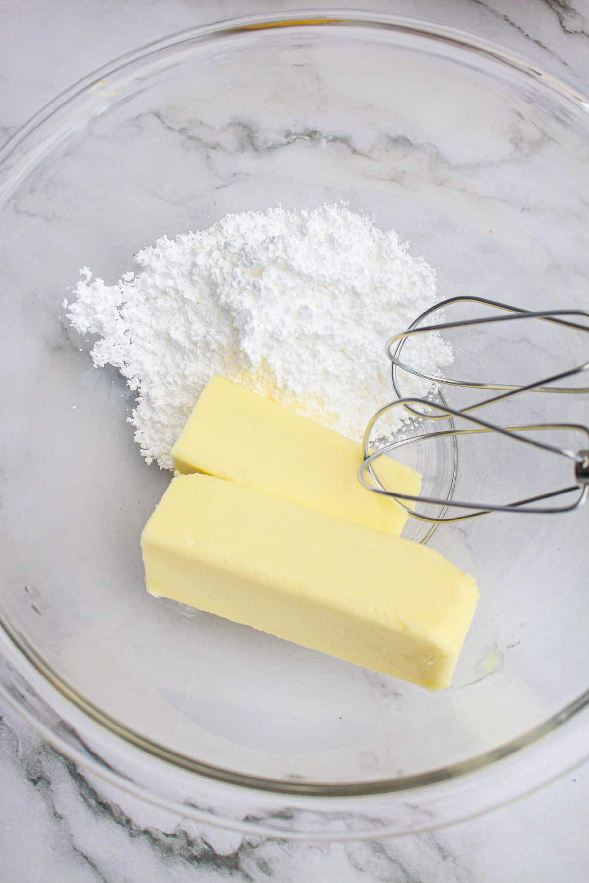 butter and powdered sugar being mixed with a hand mixer in a glass bowl.