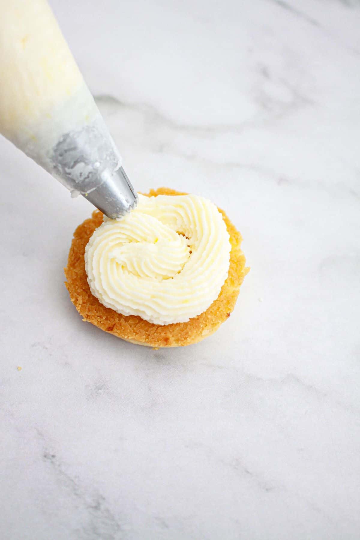 frosting being piped on top of a cookie.