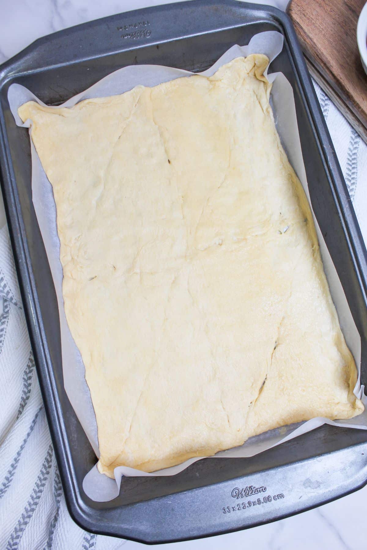 crescent roll dough spread out on a baking dish with the seams pinched together.