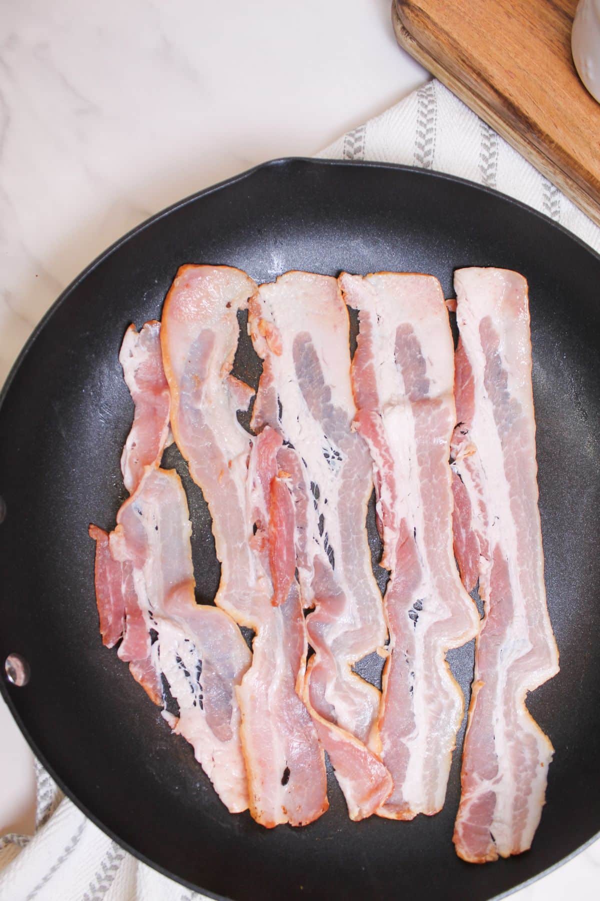 bacon being cooked in a large skillet.