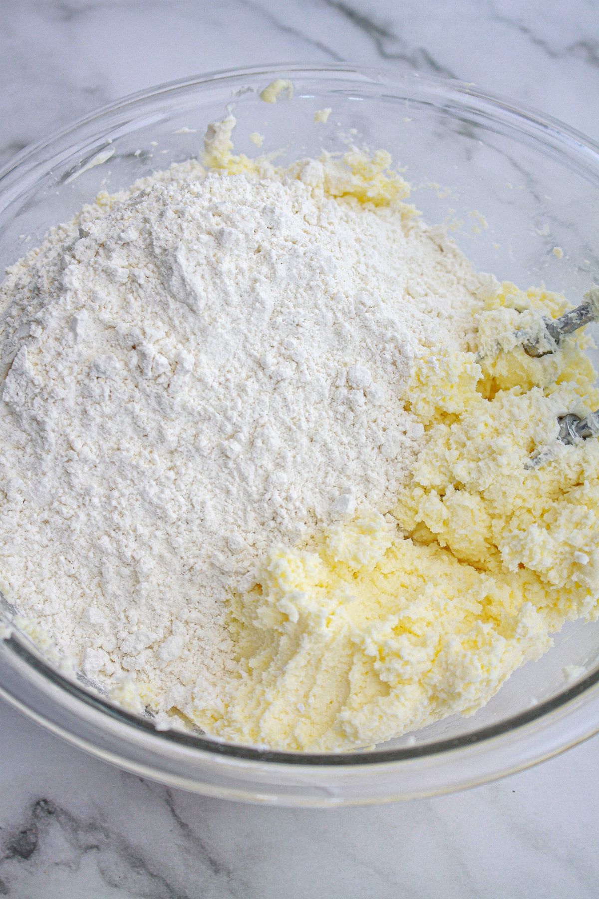 flour being mixed into cookie dough in a glass bowl with a hand mixer.