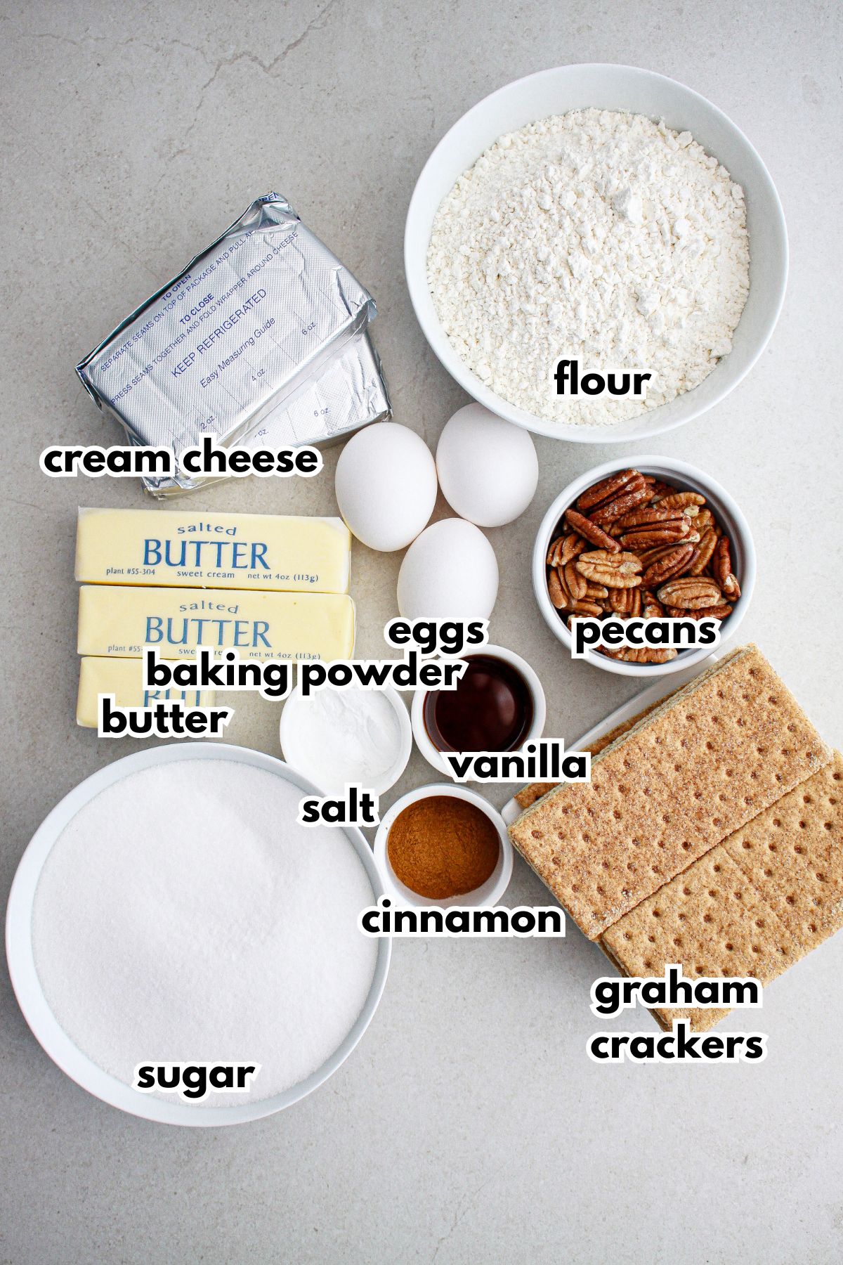 cream cheese, flour, butter, baking powder, salt, vanilla, eggs, pecans, sugar, cinnamon and graham crackers on a counter.
