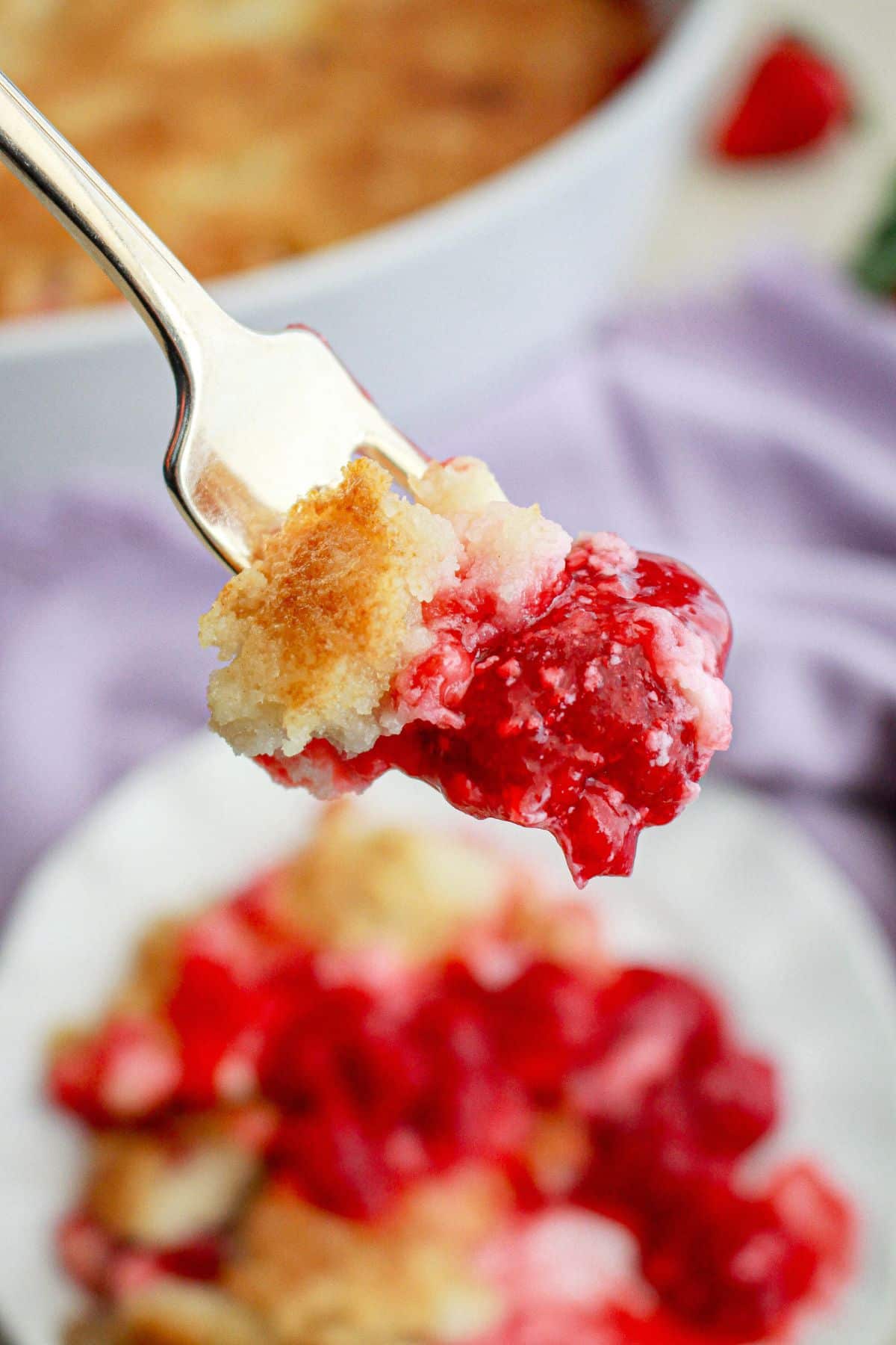 bite of strawberry dump cheesecake on a fork held in the air.