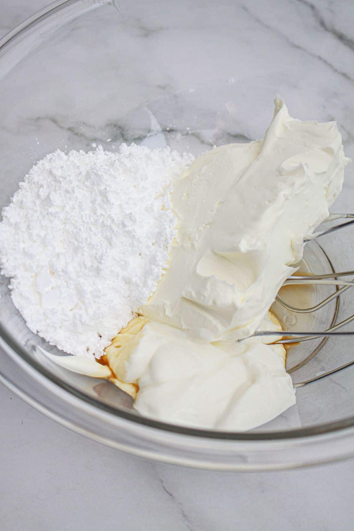 cream cheese, vanilla, and powdered sugar being mixed in a bowl.