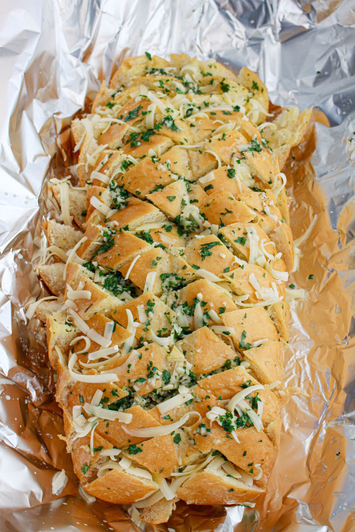 garlic butter and shredded cheese being added on top of a loaf of bread.