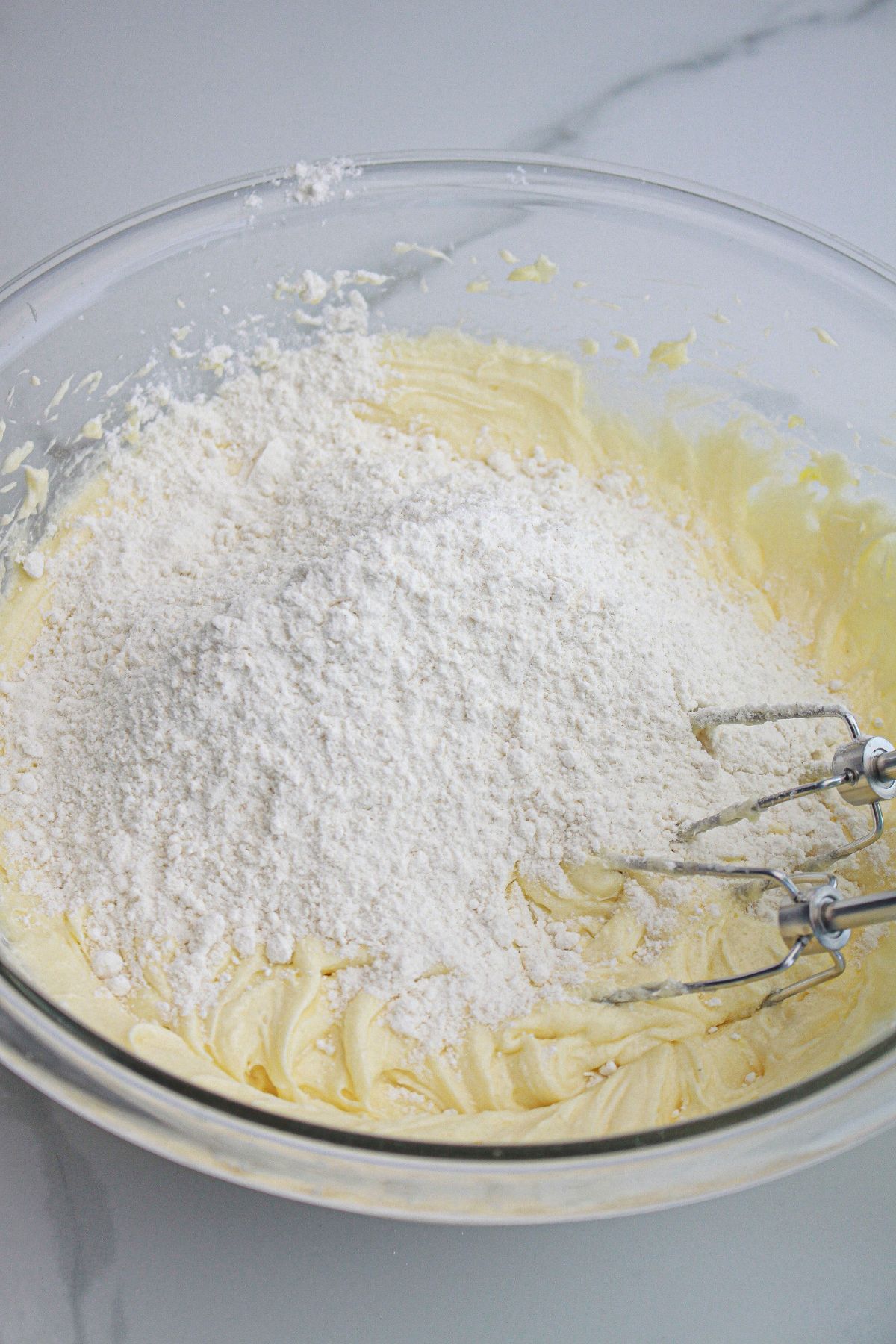 cake batter being mixed with a hand mixer in a glass bowl.