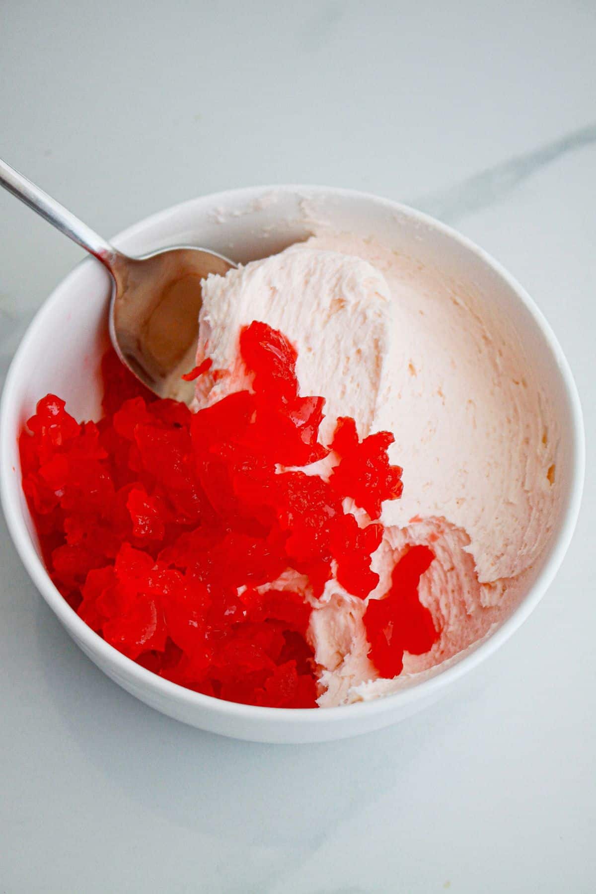 cherries being added to frosting in a small bowl.