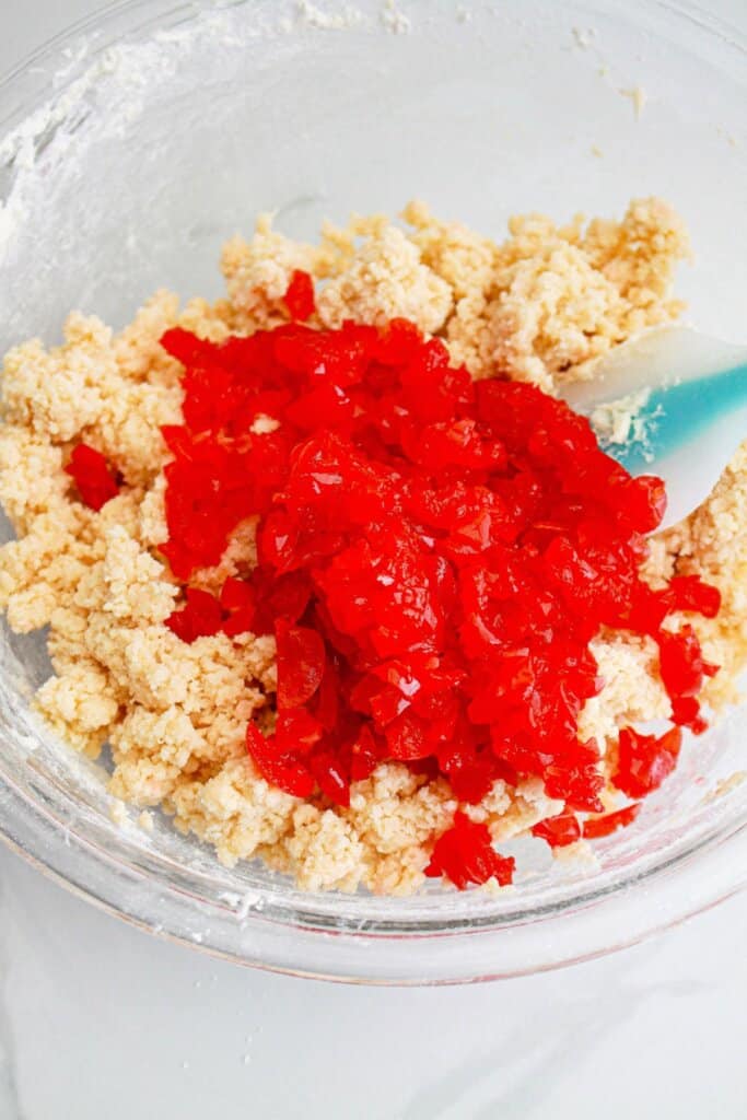 cherries being mixed into cookie dough in a glass bowl.