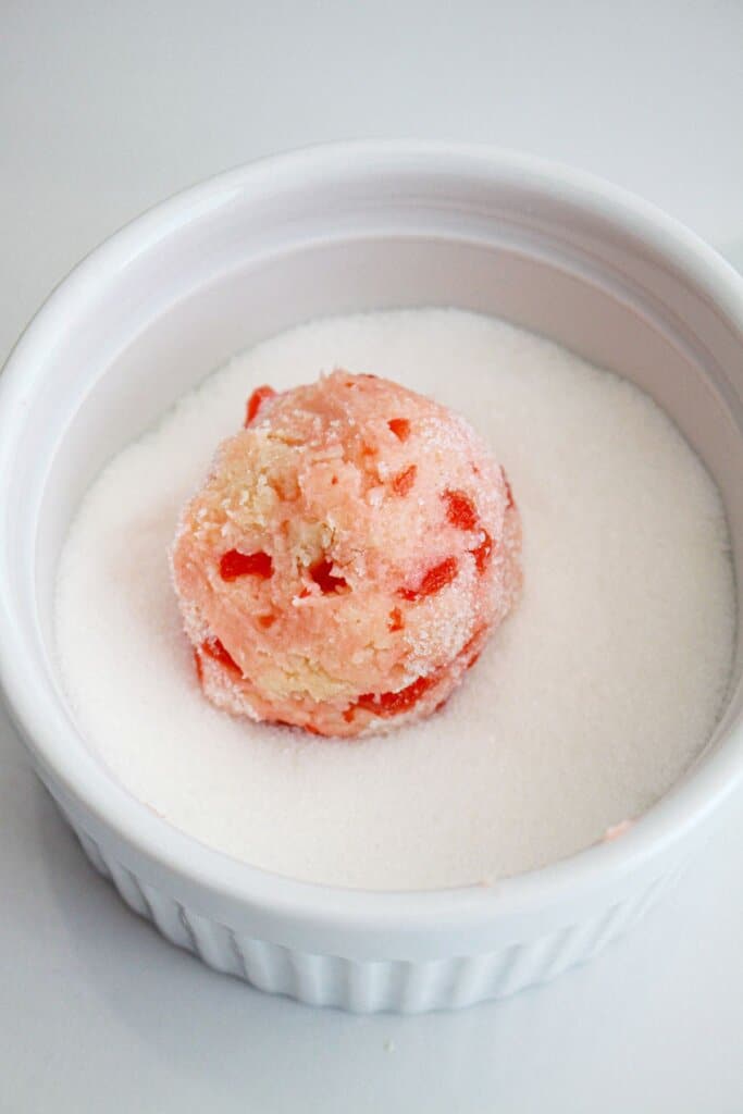 cookie dough ball being coated in granulated sugar.