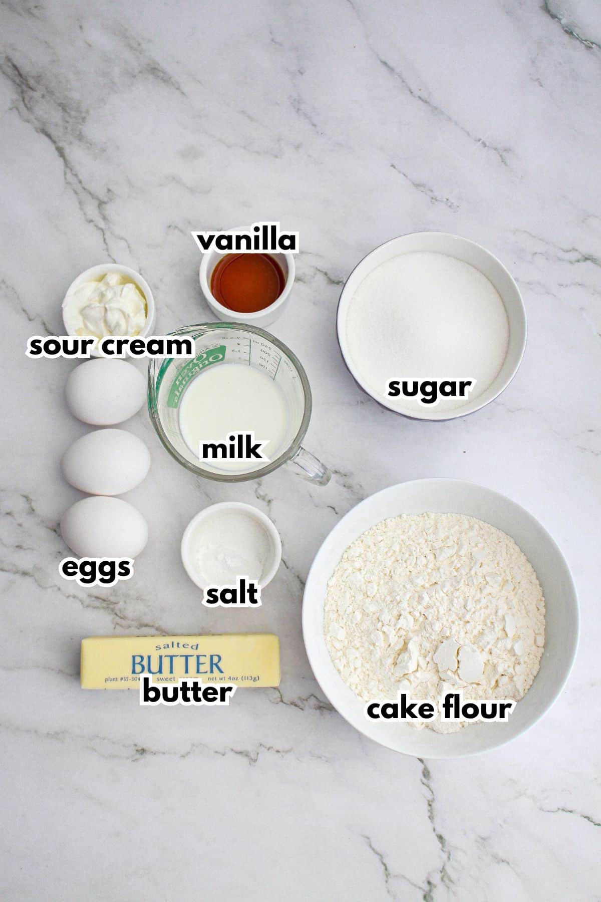 bowls of sour cream, vanilla, milk, sugar, eggs, salt, butter and cake flour on a counter.