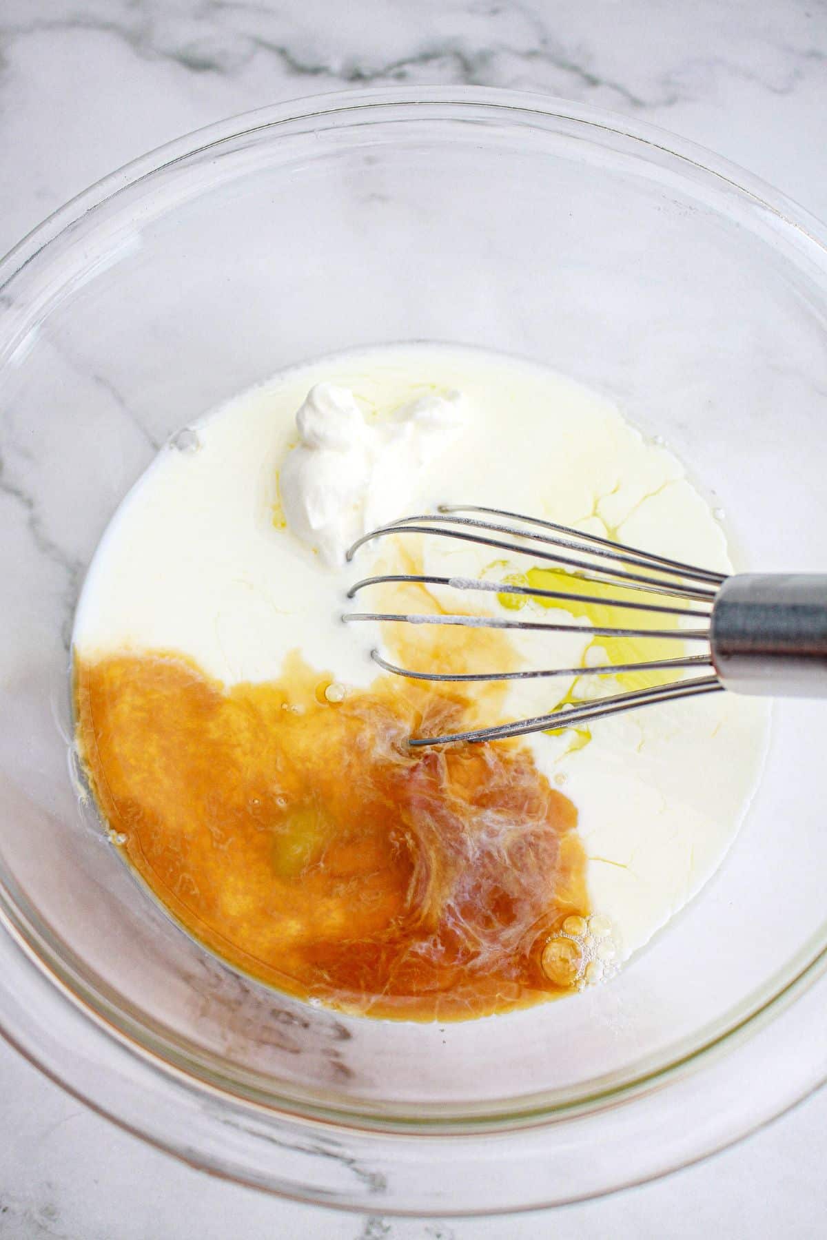 wet ingredients being mixed together with whisk in a glass bowl.