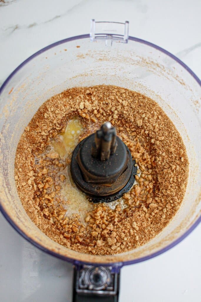 graham cracker crumbs and melted butter being mixed in a food processor.